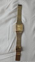 Full view of vintage gold plated watch with metal expandable bracelet on white fabric background