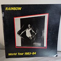 Front cover of the Rainbow World Tour 1983-84 program showing the black cover with a centered photo and text in yellow.