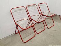 Three vintage 1980s Italian Talin metal folding chairs with red tubular frames and white grid net seats and backs, shown standing side by side.