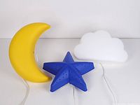 Photo showing yellow crescent moon, blue star with holes, and white cloud wall lamps with cords plugged in on white background.