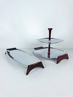 Photo showing two serving pieces: a two-tiered square tray with central handle and a long tray with wood handle accents