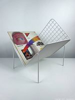 Side view showing magazine stored inside the white metal holder with mesh and perforated sides.