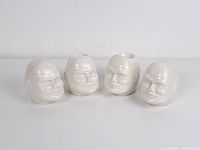 Set of four vintage ceramic head-shaped items, two with holes on top as salt and pepper shakers, two open on top as egg holders, all in white.