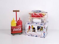 Vintage Coca-Cola condiment bottles in red metal holder alongside wooden picnic table condiment set on top of box