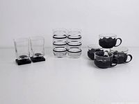 Photo showing full set of 8 items: 2 striped juice glasses, 2 square liquor glasses, and 4 black espresso cups with holders.