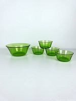 Set of five green vintage glass bowls, including one large and four smaller bowls arranged on a white surface.