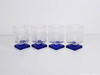 Front view of four vintage glasses with cobalt blue square bases and textured clear glass bodies arranged in a line.