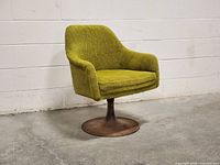 Front-left angle showing green fabric upholstery and metal pedestal base