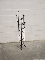 Full view of the vintage six-arm metal floor candle holder against a white wall, showing its height and structure.