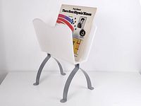 Front view showing magazine holder with record inserted, white molded plastic container with silver metal curved legs.