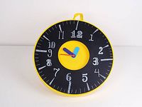 Full front view of the round yellow Ikea Pladdra wall clock showing black face with white numbers in handwritten style and colorful clock hands.