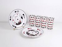 Two round plates with printed playing card designs and four playing cards in the center, alongside the four glass tumblers with playing card suit patterns.