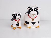 Front view of large and small porcelain cow jugs showing details of faces, collars, and golden hooves