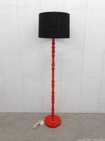 Full view of the tall red floor lamp with glossy finish and black shade on neutral background.