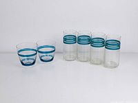 Two short glasses with turquoise stripes and four tall glasses with double turquoise bands near the rim on white background