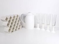 Full lot view showing the white Copco spice rack grid, Guzzini jug with gray handle and lid, and four Bodum Oktett champagne flutes with white bases.