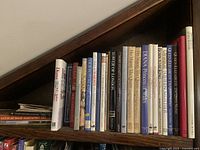 Photo showing wooden bookshelf shelf with 18 assorted books focused on royal biographies, historical events and classic literature.