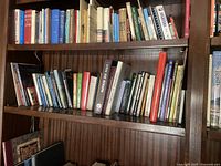 Wooden bookshelf with three shelves holding assorted books of various genres and subjects.