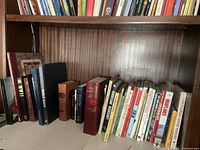 Wooden bookshelf shelf with multiple rows of assorted books including titles on history, literature and religion.