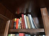 Shelf section of wooden bookshelf with books and spiral notebooks arranged vertically