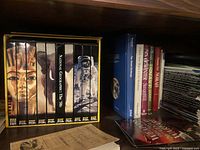 Photo of a bookshelf with a boxed set on Nabatean Ceramics, various books including anatomy and Norah, and a stack of CDs or DVDs.