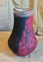 Full view of matte black vase with red feather pattern, showing shape, colour and finish