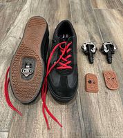 Shoe sole showing installed SPD cleat, red laces, two Shimano pedals, two cleat covers