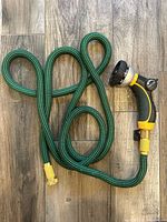 Full view of green expandable hose coiled with attached yellow/black nozzle