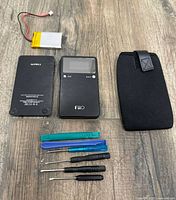 All parts laid out: amplifier body, rear cover, battery, case, pry tools, screwdrivers