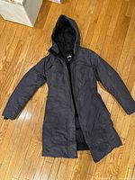 Full view of dark gray hooded long parka laid flat