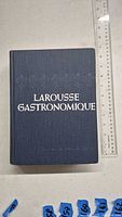 Top view showing front cover with embossed title 'LAROUSSE GASTRONOMIQUE' in white on blue hardcover.