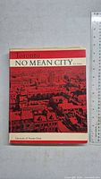 Front cover of 'No Mean City' book showing red and white design with black and white historic image of Toronto.