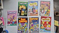 Overview photo showing all 7 comic book issues laid out on a table, featuring different Simpsons themed covers and characters.