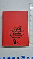 Front cover of The World Encyclopedia of Comics hardcover book with red cover, black text and cartoon cat illustration.