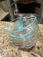 Stacked view of 5 apple-shaped glass bowls in assorted tinted colors with leaf and stem detail on the rim on a granite counter.