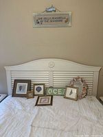 Beach-themed wall and tabletop decorations with framed seashell prints, 'OCEAN' decor, and a seashell wreath arranged on a white headboard.