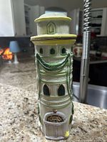 Front and side view of ceramic pasta container shaped like a tower with green garlands and yellow roof, placed on kitchen counter