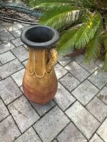 Full view of the ceramic patio vase showing the black flared rim, the snake-shaped handles, and the gradient brown to reddish body set on patio bricks.
