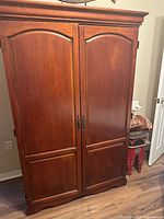 Front view of cherry wood armoire with large double doors and decorative molding.