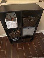 Front view of black cube shelving unit with woven and fabric baskets inside compartments placed on floor.