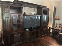 Front view of the dark wood five-piece entertainment center with the TV turned off, showing glass cabinet doors and shelving details.