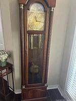 Full front view of grandfather clock showing wood case, glass door, weights and pendulum
