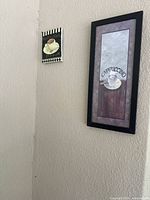 Two coffee-themed kitchen wall hangings mounted on a beige wall, one larger rectangular black-framed and one smaller square with decorative border.
