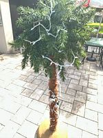 Full view of artificial palm Christmas tree with string lights on outdoor tiled floor.