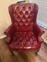 Front view of red leather wingback chair showing button-tufted seat and backrest, nailhead trim, and Queen Anne cabriole legs.