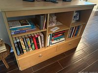 Front-right angled view of the wooden bookshelf showing compartments and drawers with visible wood grain and metallic drawer handles.