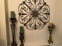 Photo showing the ornate iron wall décor with three different iron candle holders and candles.