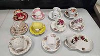 Initial photo showing all eleven china teacups with matching saucers displaying varied floral and color designs.