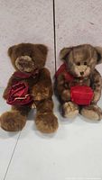Two teddy bears sitting side by side, one brown with red bow and bag, the other light brown with red scarf and gift box.