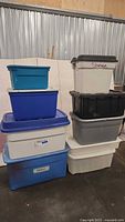 Stack of nine plastic storage totes in various colors and sizes, showing overall condition and color variation